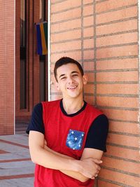 Portrait of smiling young man with arms crossed standing against wall