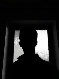 Portrait of silhouette man standing against window at home