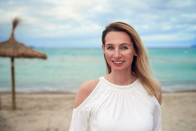 Portrait of happy mature woman standing at beach against sky