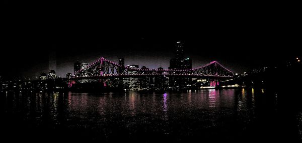 Illuminated bridge over river against sky at night