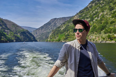 Man wearing sunglasses while standing against river and mountain