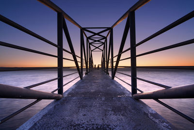 Low angle view of pier over sea against sky during sunset