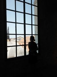 Woman looking through window while standing at home