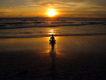 Silhouette woman sitting at beach against sky during sunset