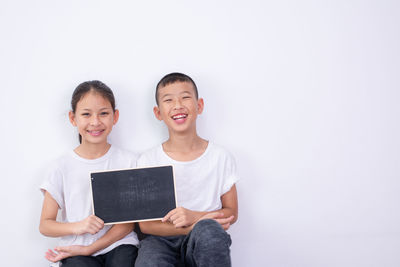 Portrait of smiling siblings holding blackboard against white background
