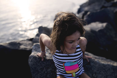 High angle view of girl sitting on rocks by sea