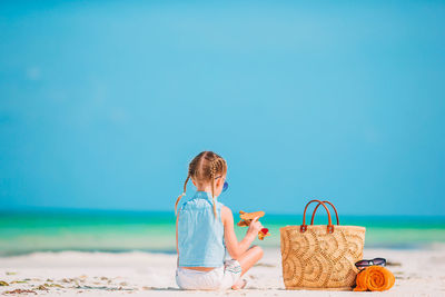 Rear view of girl on beach against blue sky
