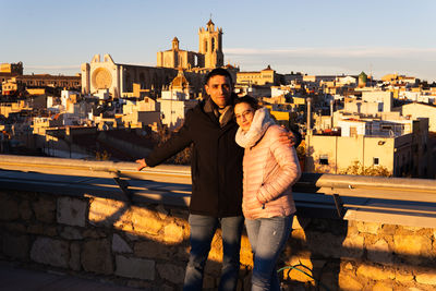 Young couple pose for a photo with the cathedral of tarragona in the background.