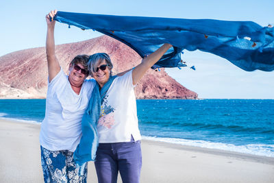 Senior woman with friend holding scarf at beach