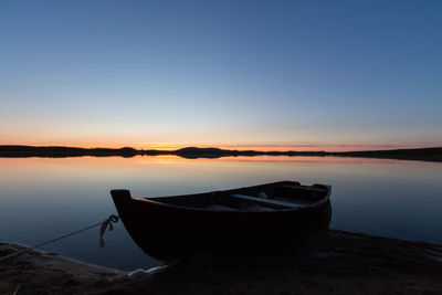 Boat moored on shore against sky during sunset