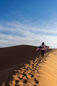 Woman on sand dune in desert against sky