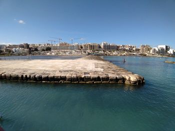 Scenic view of sea by buildings against clear blue sky