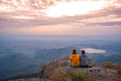 Rear view of people sitting on mountain against sky