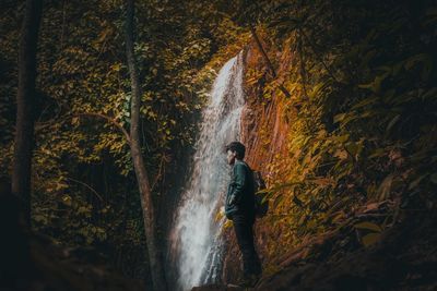Man standing by waterfall at forest