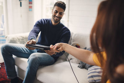 Cropped image of woman assisting man in charging digital tablet at home