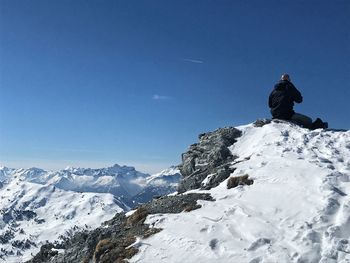 Man skiing on snowcapped mountain against clear blue sky