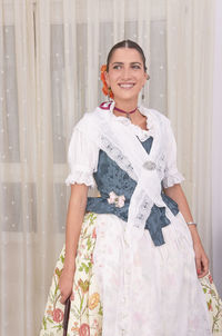 Portrait of smiling young woman standing against wall