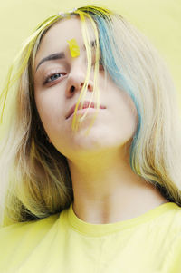Close-up of young woman with dyed hair against yellow background