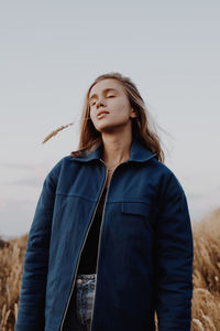 Beautiful young woman with eyes closed standing against sky