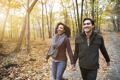 Happy couple holding hands while walking in forest