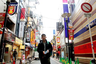 Portrait of young man standing on street amidst buildings in city