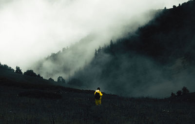 Rear view of woman standing on foggy land against mountain
