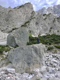 Low angle view of male hiker standing on rock against mountains