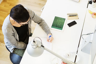 High angle view of businesswoman writing in book at desk in creative office