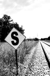 Road sign by trees against sky