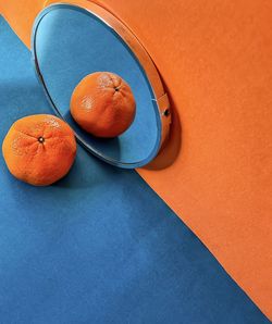 Mandarin orange on blue background reflected in mirror on orange background.
