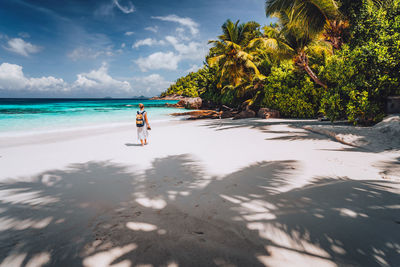 Rear view of woman with backpack walking at beach against sky