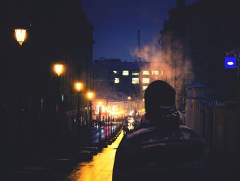 Rear view of man in illuminated city against sky at night