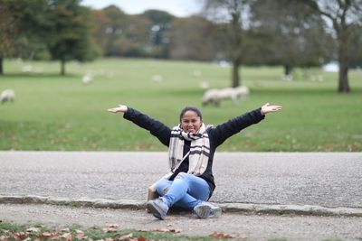 Portrait of smiling woman with arms outstretched sitting on footpath