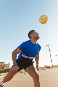 Man heading ball while playing soccer during sunny day