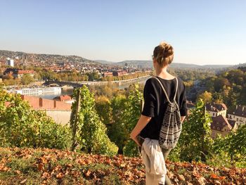 Young woman standing by tree in city against clear sky