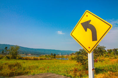 Road sign on field against clear blue sky