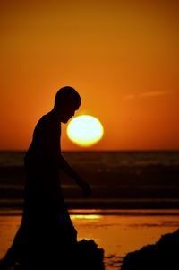 Silhouette woman standing by sea against orange sky