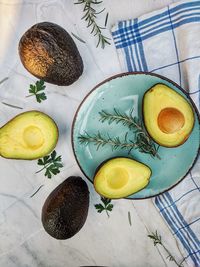 Fresh avocado with herbs and lemons lies on the table on blue plate on white background. flat lay