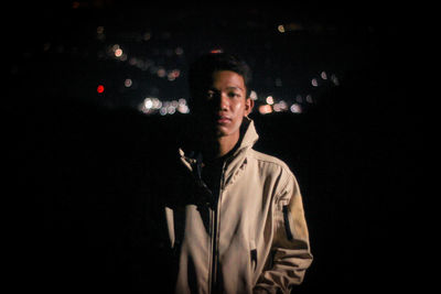 Portrait of young man standing against black background