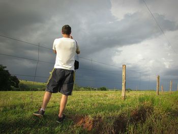 Rear view of man standing on grassland against cloudy sky