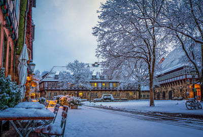 Snow covered street by buildings in city against sky