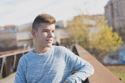 Thoughtful teenage boy standing on footbridge in city