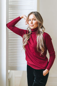  beautiful woman with blonde long curly hair in bordo sweater in bright interior, winter warm clothes