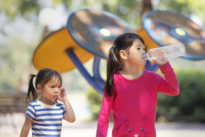 Cute girl drinking water while standing with sister at park