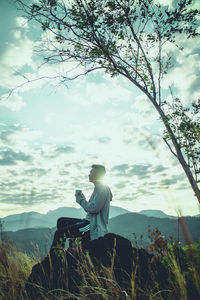 Statue of man sitting by plants against sky