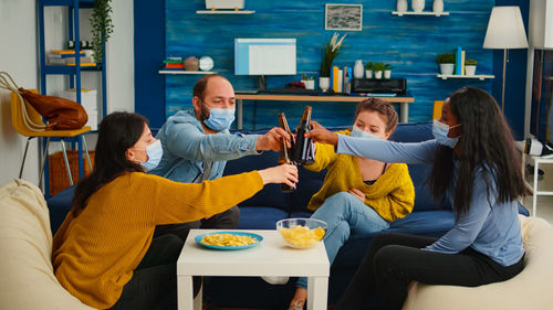 Cheerful people wearing mask holding beer at home