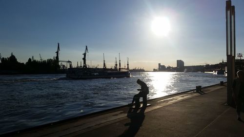 Silhouette of industrial ship on river with commercial dock against sky