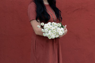 Woman holding white flower against wall