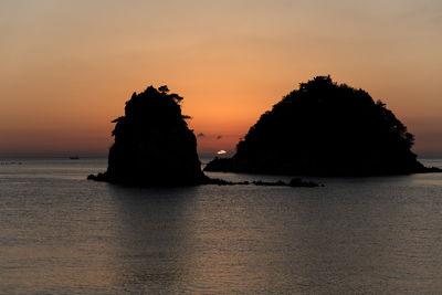 Rock formation in sea against sky during sunset