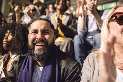 Portrait of happy man with sports scarf around neck sitting in stadium on sunny day